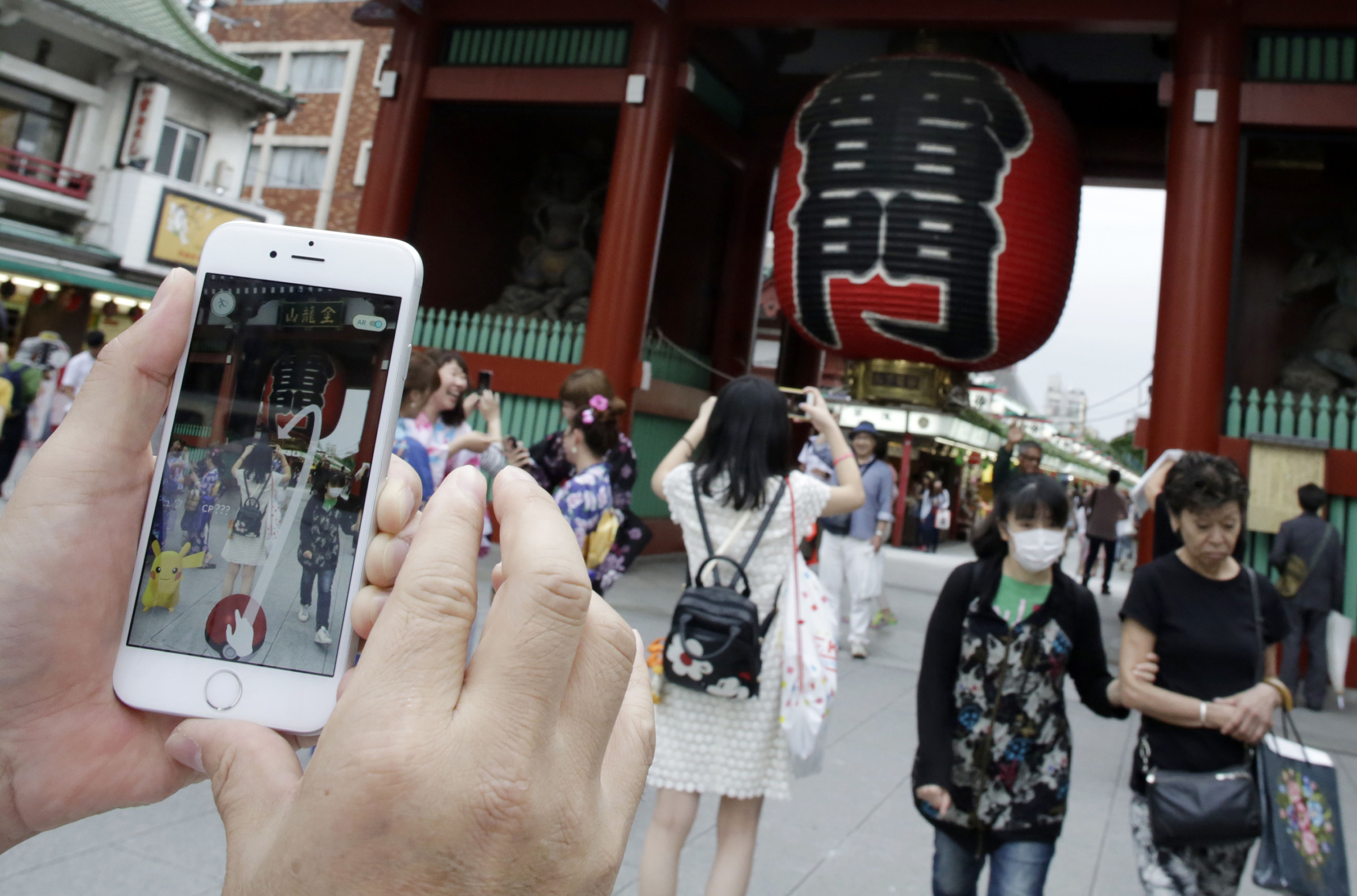 A man tries to catch a Pikachu, a Pokemon character, while he plays "Pokemon Go" in front of Kaminarimon, or Thunder Gate, at the Sensoji temple in Tokyo's Asakusa shopping and tourist district, Friday, July 22, 2016. Users began tweeting it was available Friday morning, and the Pokemon Co. and the developer of the augmented reality game, U.S.-based Niantic Inc., confirmed its launch shortly after. (AP Photo/Eugene Hoshiko)