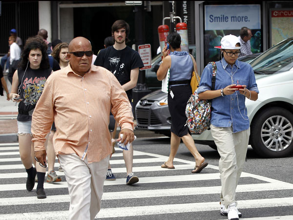 Pedestrians cross a street in downtown Washington in this July 2012 file photo. Across the country on city streets, in suburban parking lots and in shopping centers, there is usually someone strolling while talking on a phone, texting with their head down, listening to music, or playing a video game. AP 