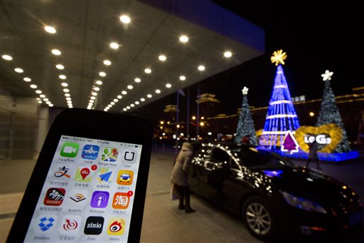The Uber app is displayed on a phone posed for photos near a woman peering into a car outside a office building in Beijing, Friday, Jan. 9, 2015. China has banned drivers of private cars from offering services through ride-hailing apps, throwing up a new hurdle to Uber Technologies Ltd.'s global expansion. (AP Photo/Ng Han Guan)
