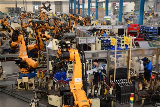 In this June 26, 2015 photo, workers assemble parts next to robot arms at an auto parts manufacture factory in Dafeng city in east China's Jiangsu province. For decades, China's manufacturers employed waves of young migrant workers from the countryside to work at countless factories in coastal provinces, churning out cheap toys, clothing and electronics. Now, factories are rapidly replacing those workers with automation, a pivot that’s encouraged by rising wages and new official directives aimed at helping the country move away from low-cost manufacturing. (Chinatopix via AP) CHINA OUT