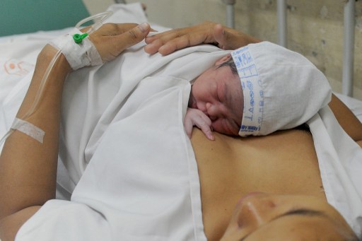 A newborn baby is placed on his mother seconds after birth at the Fabella government maternity hospital in Manila on March 4, 2015, during the 'First Embrace' campaign for Early Essential Newborn Care of the World Health Organization (WHO).  "First Embrace" refers to sustained skin-to-skin contact immediately after birth. This simple act of affection transfers life-saving warmth, placental blood and protective bacteria from mother to newborn.   AFP PHOTO / Jay DIRECTO / AFP PHOTO / JAY DIRECTO