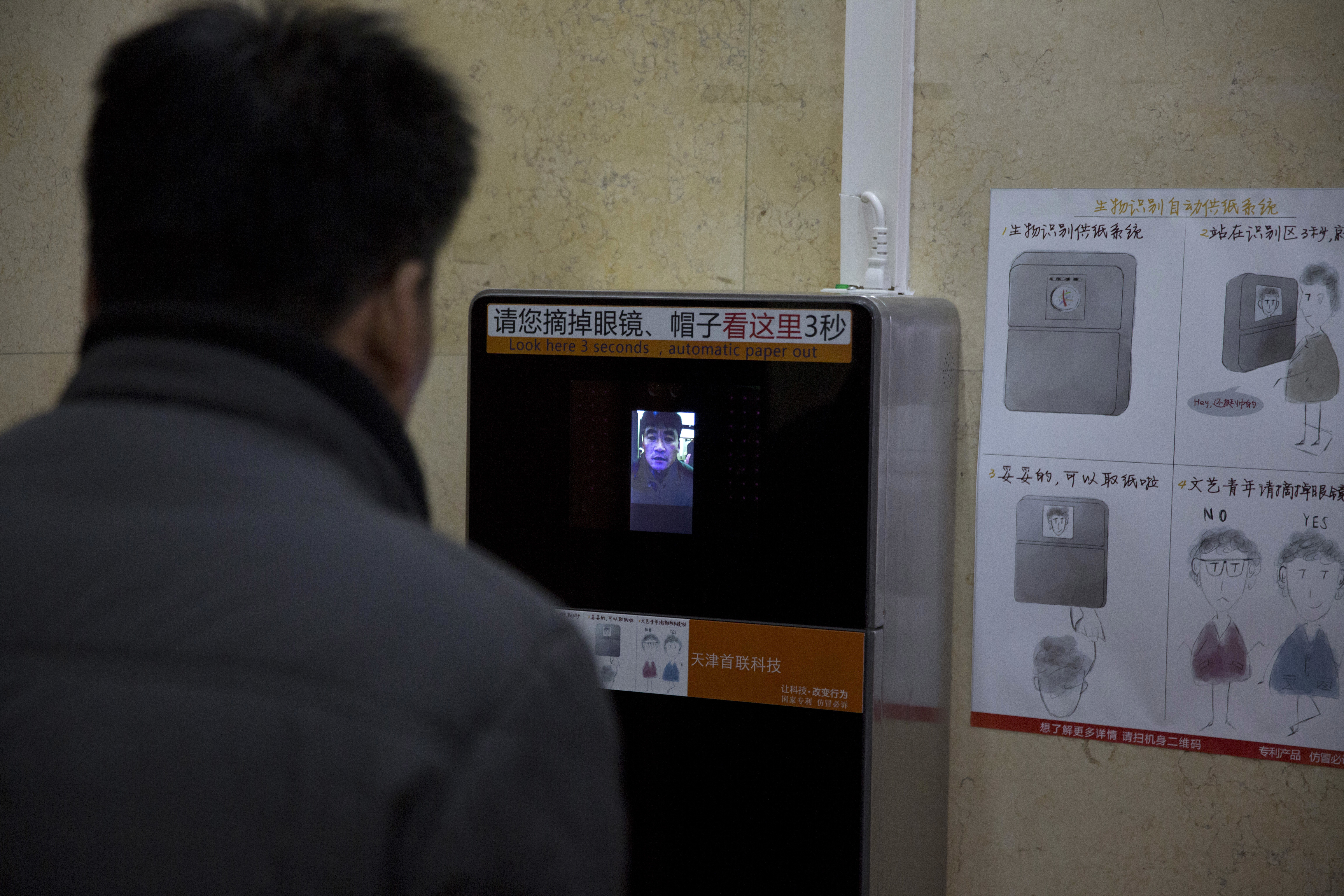 In this photo taken Tuesday, March 21, 2017, a man tries out a facial recognition toilet paper dispenser at a toilet in the Temple of Heaven park in Beijing, China. At Beijing's 600-year-old Temple of Heaven, administrators recognized the need to stock the public bathrooms with toilet paper, a requirement for obtaining a top rating from the National Tourism Authority. But they needed a means of preventing patrons from stripping them bare for personal use - hence the introduction of new technology that dispenses just one 60-centimeter (2-foot) section of paper every nine minutes following a face scan. (AP Photo/Ng Han Guan)
