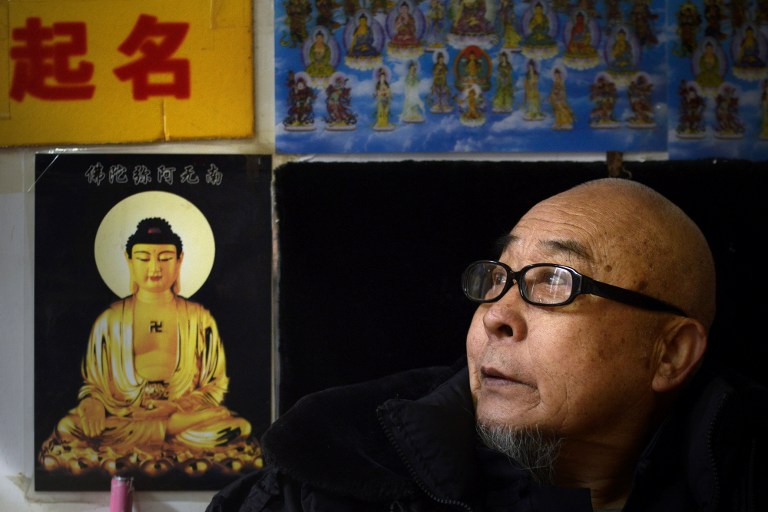 This picture taken on February 28, 2017 shows fortune-teller Mao Shandong looking on as he waits for customers in his shop in Beijing. In a one-room shop tucked inside a Beijing alley, a bearded 74-year-old fortune-teller in crimson tunic offers what Chinese parents have sought for centuries: an auspicious name for their newborn. But business has been tough lately for Mao Shandong and others in his trade as tech-savvy entrepreneurs have turned the ancient naming tradition into a lucrative online business.  / AFP PHOTO / WANG Zhao / TO GO WITH China-lifestyle-economy-tradition-culture-naming, FEATURE by Yanan WANG