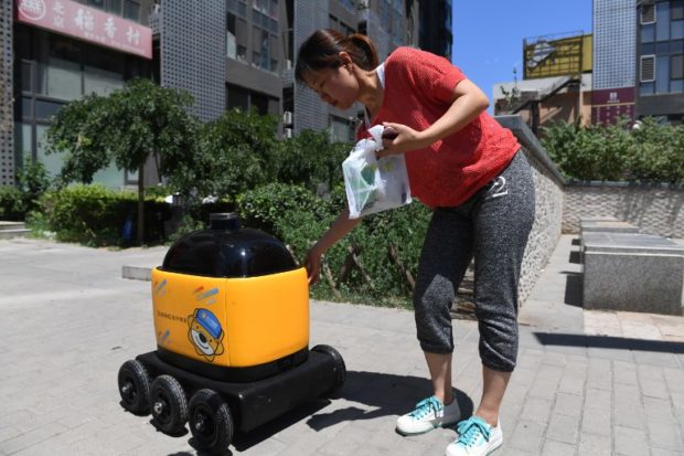 china A woman picks up groceries delivered by a Zhen Robotics delivery robot at a residential compound during a demonstration of the robot in Beijing. Along a quiet residential street on the outer edges of Beijing, a yellow and black cube about the size of a small washing machine trundles leisurely to its destination. This "little yellow horse" is an autonomous delivery robot, ferrying daily essentials like drinks, fruit and snacks from the local store to the residents of the "Kafka" compound in the Chinese capital.  / AFP PHOTO / GREG BAKER / TO GO WITH AFP STORY CHINA-TECHNOLOGY-ROBOTS-CONSUMER-SCIENCE,FEATURE BY LUDOVIC EHRET