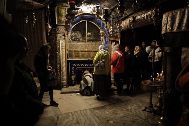 A group of tourists and pilgrims visit the Grotto, believed to be the exact spot where Jesus Christ was born, as others pray at the Church of the Nativity in the occupied West Bank biblical city of Bethlehem, on December 12, 2018. - Bethlehem is buzzing, with more tourists expected this Christmas than have visited in years, but it is causing some unexpected problems. Such are the crowds at the church built on the site where Jesus is believed to have been born that the authorities are planning to introduce an advance reservation system through an app. (Photo by THOMAS COEX / AFP)