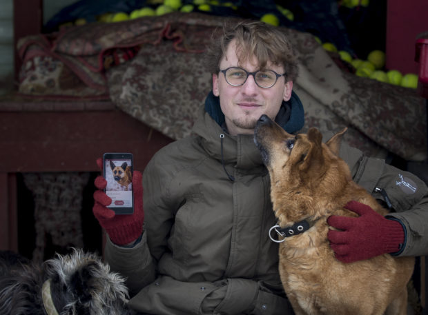 In this photo taken on Saturday, Feb. 2, 2019, Vaidas Gecevicius, who developed an app helping to match stray dogs with potential owners, poses for a picture with a dog and shows this dog's profile on the app in Vilnius, Lithuania.  A group of enthusiasts have launched an app that helps match aspiring dog owners with stray dogs. (AP Photo/Mindaugas Kulbis)