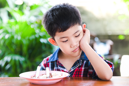 asian little boy boring eating with rice food on the wooden table