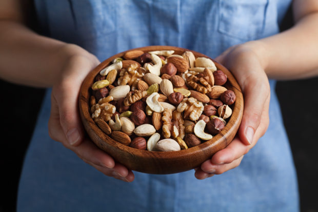 Womans hands holding bowl with nuts. Walnut, pistachios, almonds, hazelnuts