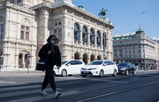 A woman with a protection mask crosses a street at the Vienna