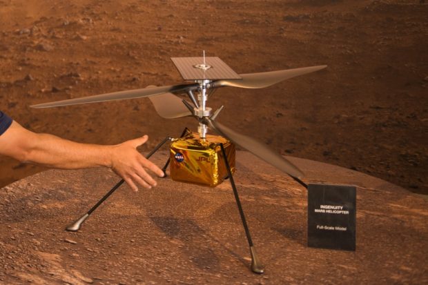 A staff member places a full-scale model of the Ingenuity Mars Helicopter at NASA's Jet Propulsion Laboratory (JPL) on a table ahead of the Mars 2020 Perseverance rover landing on February 18, 2021 in Pasadena, California. - The Mars exploration rover will search for signs of ancient microbial life and collect rock samples for future return to Earth to study the red planet's geology and climate, paving the way for human exploration. Perseverance also carries the experimental Ingenuity Mars Helicopter - which will attempt the first powered, controlled flight on another planet