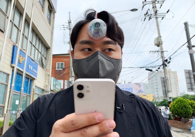 South Korean industrial designer Paeng Min-wook showcases a robotic eye, called "The Third Eye", on his forehead as he uses his mobile phone while walking on street, in Seoul, South Korea, March 31, 2021. Picture taken on March 31, 2021. REUTERS/Minwoo Park