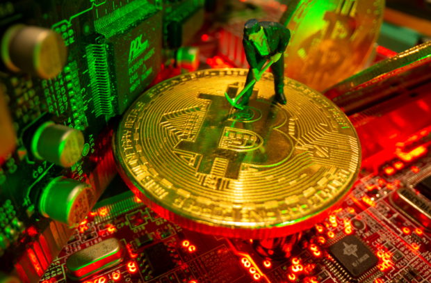 A small toy figure and representations of the virtual currency Bitcoin stand on a motherboard in this picture illustration
