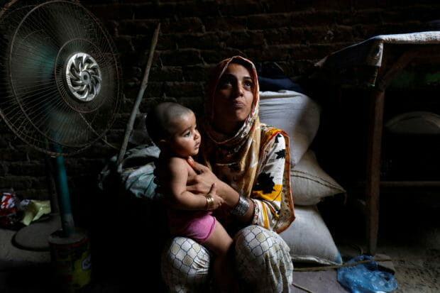 Razia, 25, and her six-month-old daughter Tamanna, sit in front of a fan to cool off during a heatwave, in Jacobabad, Pakistan, May 15, 2022. Last month Jacobabad became the hottest city on Earth. Women are especially vulnerable to rising temperatures in poor countries on the frontlines of climate change because many have little choice but to work through their pregnancies and soon after giving birth, according to interviews with more than a dozen female residents in the Jacobabad area as well as half a dozen development and human rights experts.  REUTERS/Akhtar Soomro